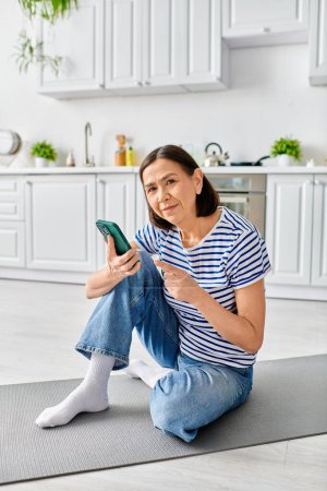A woman in cozy homewear sits on the floor, engrossed in her cell phone.