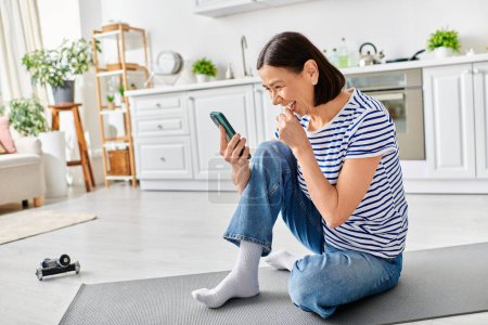 A mature, beautiful woman in cozy homewear sits on the floor, engrossed in her cell phone.