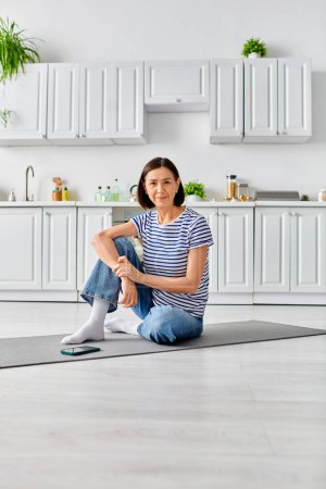 Mature woman in cozy homewear practicing yoga on a mat in a kitchen setting.