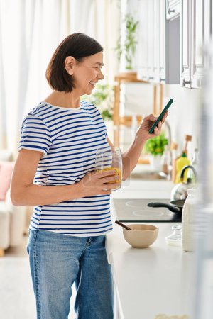 A woman in cozy homewear enjoys a glass of orange juice in her kitchen.