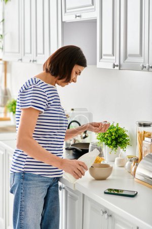 A woman in cozy attire stands in a kitchen, preparing food with focus and skill.
