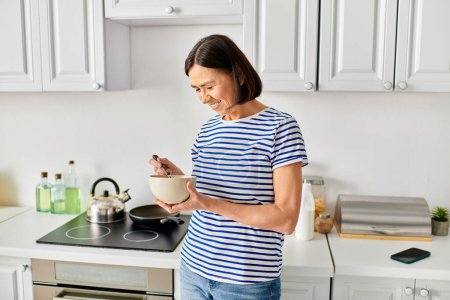 Mature woman in cozy homewear holding a bowl of food in a kitchen.
