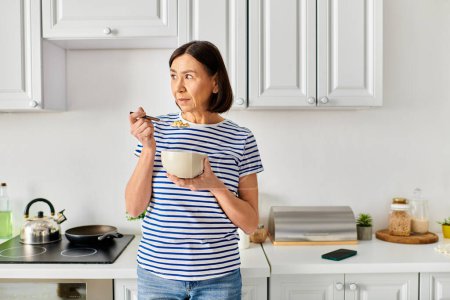 Stylish woman in cozy attire holding a bowl of food in a warm kitchen.