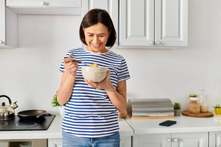 A mature woman in cozy homewear holding a bowl of food in a kitchen.