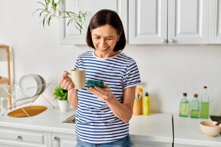 Una mujer en ropa de casa acogedora sosteniendo una taza, absorta en su teléfono celular.