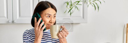 Foto de Una mujer en acogedora multitarea de ropa de casa con un teléfono celular y una taza de café. - Imagen libre de derechos
