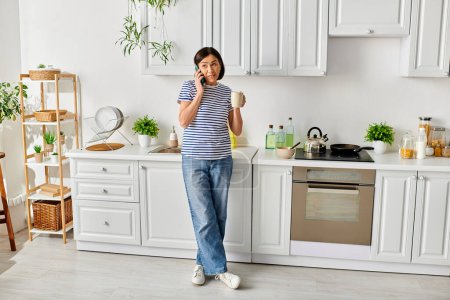 Foto de Una mujer en ropa de casa acogedora hablando en un teléfono celular en una cocina. - Imagen libre de derechos