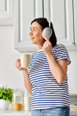A woman in cozy homewear holding a cup and hair dryer.