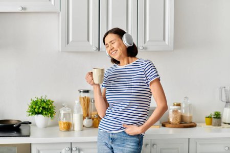 A woman in cozy homewear standing in a kitchen, holding a cup of coffee.