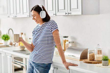 A woman with headphones stands in a cozy kitchen.