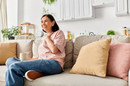 Téléchargez les photos : A mature woman in cozy homewear sitting on a couch, enjoying a cup of coffee. - en image libre de droit