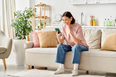 Photo for A mature woman in home attire sits on a couch, engrossed in her phone. - Royalty Free Image
