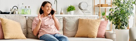 Eine reife Frau in Hauskleidung sitzt auf einer Couch und führt ein Telefongespräch.