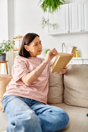 A mature woman engrossed in a book while sitting on a cozy couch at home.