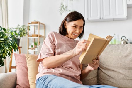 A mature, appealing woman in homewear, lost in the pages of a book while seated on a comfortable couch.
