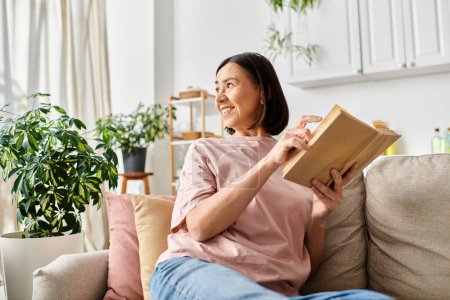 A mature woman in homewear reads a book comfortably on a couch at home.