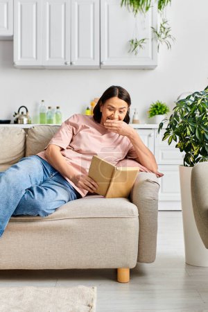 Téléchargez les photos : Femme en tenue confortable assise sur un canapé, profondément absorbée par la lecture d'un livre. - en image libre de droit