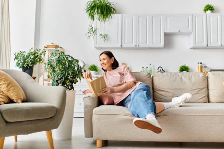 Téléchargez les photos : A woman in cozy homewear sitting on a couch, immersed in a book. - en image libre de droit