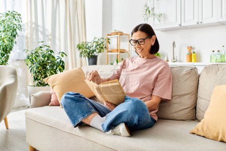 Reife Frau in gemütlicher Kleidung in ein Buch vertieft, während sie auf einer bequemen Couch sitzt.
