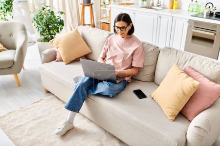Una mujer madura en ropa de casa acogedora se sienta en un sofá, totalmente centrado en su computadora portátil.
