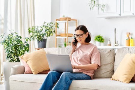 A woman in casual attire using a laptop on a couch.