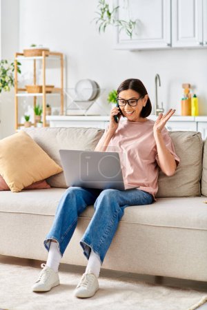 Téléchargez les photos : Une femme mûre en tenue de maison élégante s'assoit sur un canapé, absorbée dans son ordinateur portable. - en image libre de droit