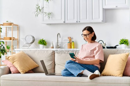 Woman in cozy homewear using laptop on couch.