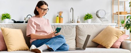Photo for Mature woman in cozy homewear sits on couch, engrossed in her phone. - Royalty Free Image