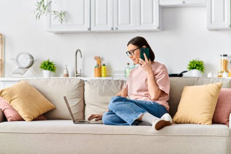 Eine reife Frau in bequemer Homewear sitzt auf einer Couch und führt ein Telefongespräch.