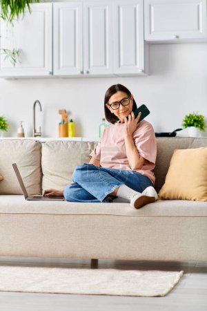 A woman in cozy homewear sits on a couch, engaged in a phone conversation.