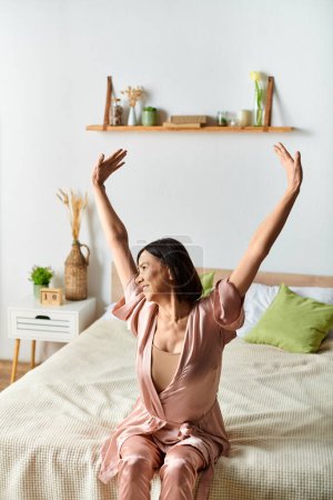 Photo for Woman sitting on bed with arms raised in joy. - Royalty Free Image