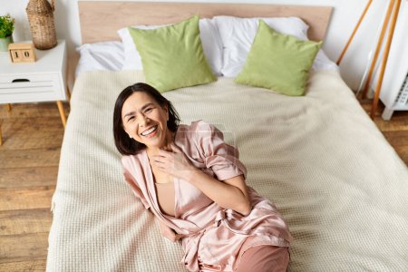 Femme mûre se détend sur un lit rose en robe confortable.