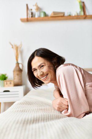 Téléchargez les photos : Une femme mûre en tenue confortable se détend sur un lit blanc. - en image libre de droit