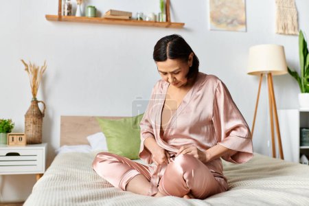 Eine reife Frau im rosa Pyjama sitzt bequem auf einem Bett.