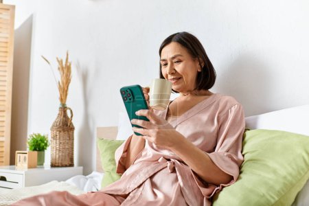 A woman in cozy homewear sitting on a bed, engrossed in her cell phone.