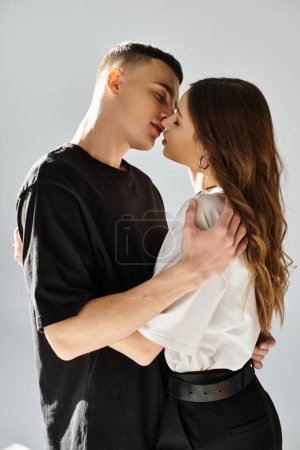A young man and woman intimately kiss each other in a studio setting with a grey background.