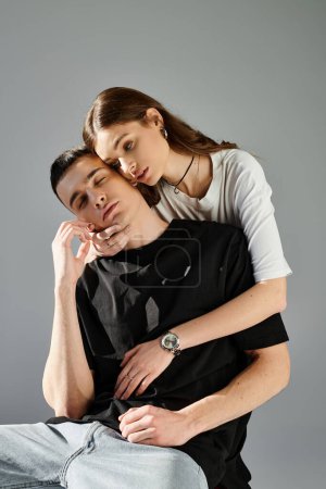 A young man balances precariously on top of a womans shoulder in a studio with a grey background.
