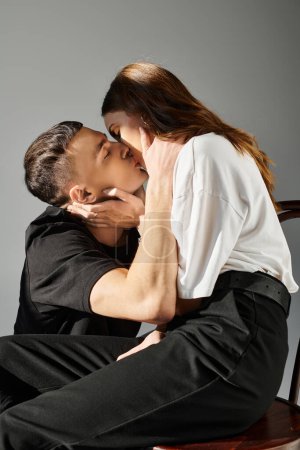 Un hombre y una mujer besándose apasionadamente en un ambiente de estudio, envueltos en amor y conexión contra un fondo gris.