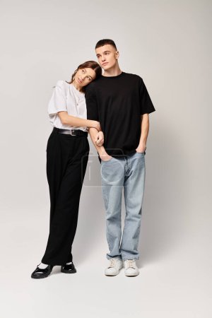 Téléchargez les photos : A young couple in love standing together in a studio, sharing a tender moment against a grey background. - en image libre de droit