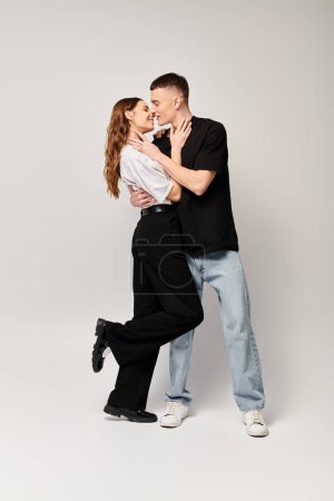 A man and a woman, young couple, dancing together in a studio with a grey background, showing love and harmony.