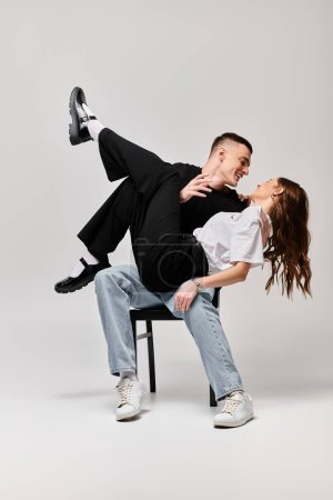 Téléchargez les photos : Un jeune couple s'assoit confortablement sur une chaise, leurs corps serrés, respirant l'amour et la tranquillité dans un studio au fond gris. - en image libre de droit