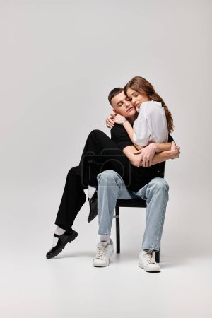 A young man and woman sit intertwined on a chair, their gazes locked in a moment of shared connection and love.