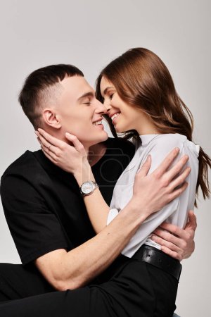 A man and a woman hugging each other affectionately in a studio with a grey background.