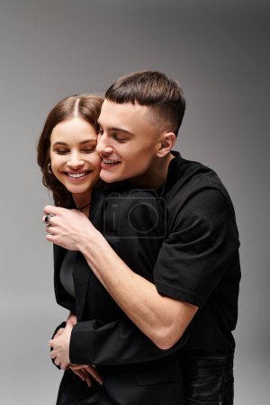A man and a woman cuddle each other warmly, their bodies intertwined in a loving embrace in a studio against a grey backdrop.