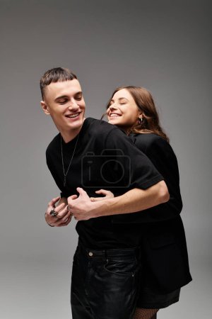 A young couple tenderly embraces each other against a neutral grey backdrop, showing affection and unity in their relationship.