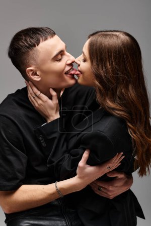 A young man and woman lock lips in a passionate kiss against a grey studio backdrop.