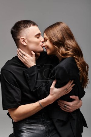 Un joven y una mujer enamorados se abrazan tiernamente en un estudio con un fondo gris.