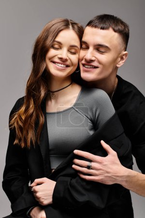 A young man and woman lovingly embrace each other in a studio setting with a grey background.