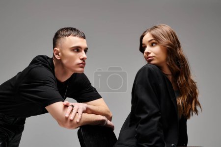 Foto de Un joven y una joven se sientan lado a lado, compartiendo un momento de cercanía y conexión en un estudio con un fondo gris. - Imagen libre de derechos