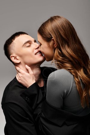 A man gently kisses a woman on the cheek, showing affection in a studio setting with a grey background.